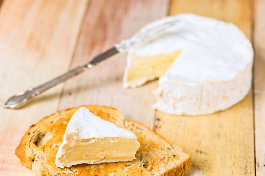 Camembert cheese with cut wedge on toasted bread slice and vinta
