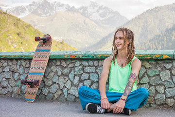 Portrait of cool, funny handsome man with skateboard at mountain