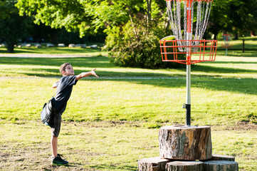 young boy playing disc golf in a park