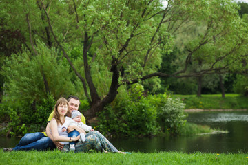 Happy family with a baby resting in summer park on the lake