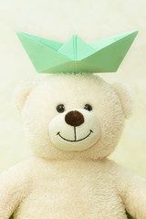 White teddy bear with a paper boat on a head