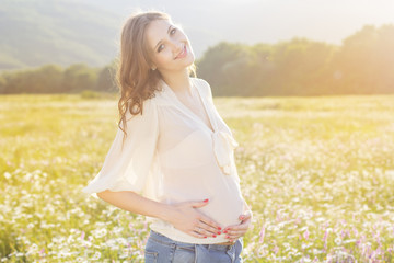 Pregnant woman standing in field behind sunset lights