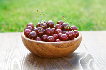 Wooden plate full with ripe red cherries in sun flare