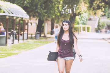 Fototapeta premium Beautiful girl walking at park holding a skateboard.
