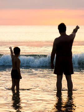 Silhouette von Vater und Sohn vor Abendhimmel am Meer