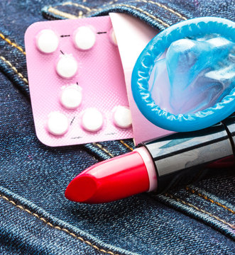 Closeup oral contraceptive pills, condom and red lipstick.