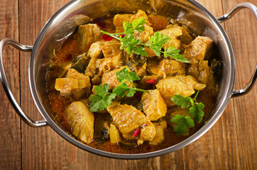 Chicken curry in  balti dish on a rustic wooden table.