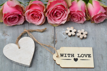 Row of pink yellow roses with label and heart shape decoration on a old wooden grey background