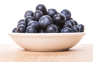 Blueberry fruits in a white bowl on wooden board background