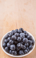 Blueberry fruits in a white bowl on wooden board background