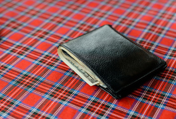 Black purse with money on plaid background