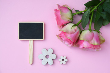 Pink painted wooden background with empty black chalk board and pink roses and flower decoration