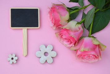 Pink painted wooden background with empty black chalk board and pink roses and flower decoration