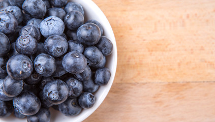 Blueberry fruits in a white bowl on wooden board background