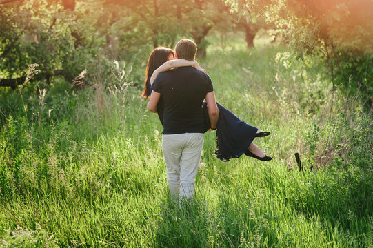 A Young Man Carries A Girl In Her Arms At Sunset In Nature, Love, Life Style