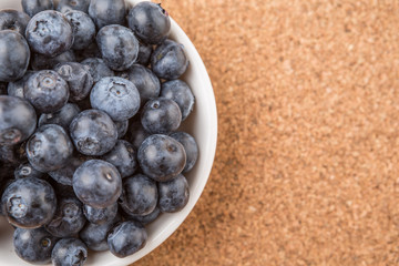 Blueberry in a white bowl on cork board background