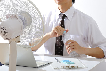 暑いオフィスで水分補給をしながら仕事をするビジネスマン