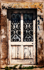 An old and worse-for-wear wooden door with wrought iron decorative windows