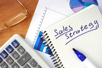 Notepad with  Sales  strategy concept on a wood board.