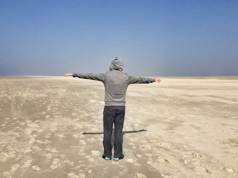 Rear view of a man in a hoodie with outstretched arms standing on a beach, Fanoe, Jutland, Denmark