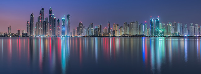 View into land of the city skyline at night with colourful lights reflected in the Persian Gulf, Dubai, UAE