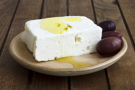 Greek feta cheese, oil, kalamata olives on rustic plate board.