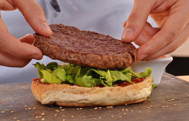 Manos de cocinero preparando hamburguesa en una cocina.