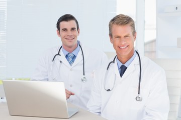 Smiling doctors looking at camera in front of laptop 