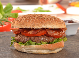 Hamburguesa con tocineta e ingredientes en la plancha.