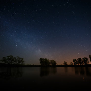 Smooth surface of forest lake on a background of the night sky 