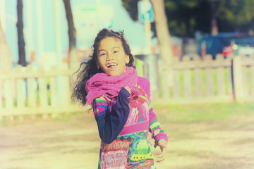 Fototapeta premium Adorable girl in colorful dress running in park sunny day. Beautiful smiling female child with long black curly hair outside in summer, image is filtered for vintage effect