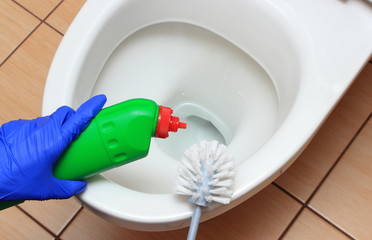 Hand of woman in blue glove cleaning toilet bowl