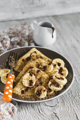 pancakes with bananas and chocolate sauce on a light wooden background
