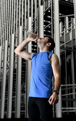 young sport man drinking water bottle after running urban training