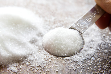 Close-up of granulated sugar in spoon and sugar pile on wooden