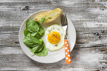 fried egg and fresh spinach on a white plate on a light wooden background
