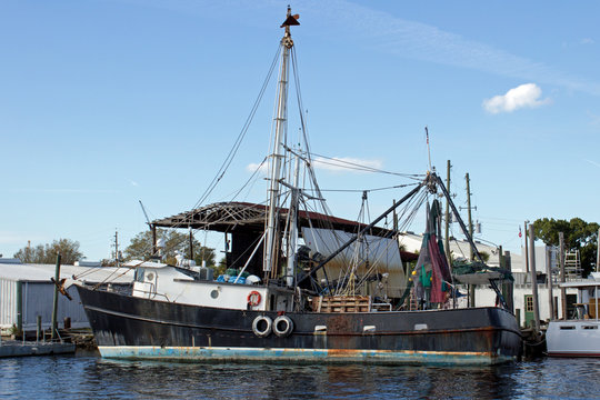 Black Fishing Boat Side - Rusty Black Fishing Boat with Tall Mast and Life Preservers Floating in Water at a Dock in Tarpon Springs Florida.