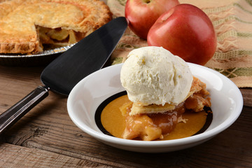 Closeup of a slice of Apple Pie a la Mode. Fresh Fuji apples and a whole pie are in the background.