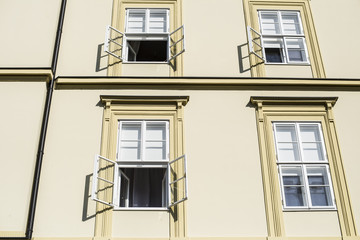 Sunlit wall of office building in the morning with open windows half of windows covered with sunshades
