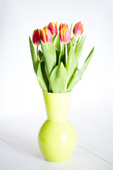 A round green vase full of tulips and leaves