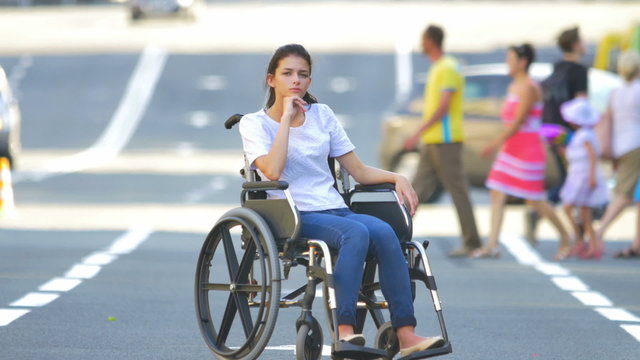 The invalid girl sit in the wheel chair in the center of the city by people and car traffic background