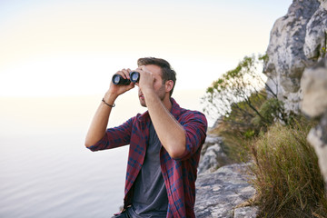 Young man on a rocky mountainside with binoculars