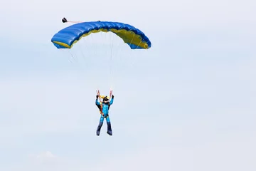 Foto auf Leinwand Parachutist in a blue suit on blue yellow parachute © Aleksei Lazukov