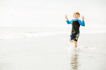Young boy in swimming shorts and rushwest runs along Bali beach