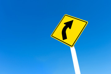 Yellow traffic right curve sign on blue sky background.
