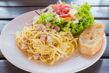 Spaghetti pasta with ham and cream sauce with salad and bread.