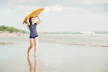 Fototapeta na wymiar Beautiful sexy surfer girl on the beach at sunset walks along