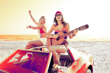 girls having fun playing guitar on th beach in a car