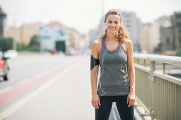 Fototapeta premium Smiling woman jogger standing still on bridge