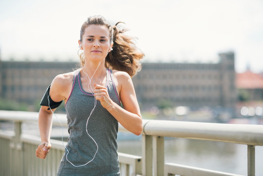 Smiling woman jogging in urban setting listening to music